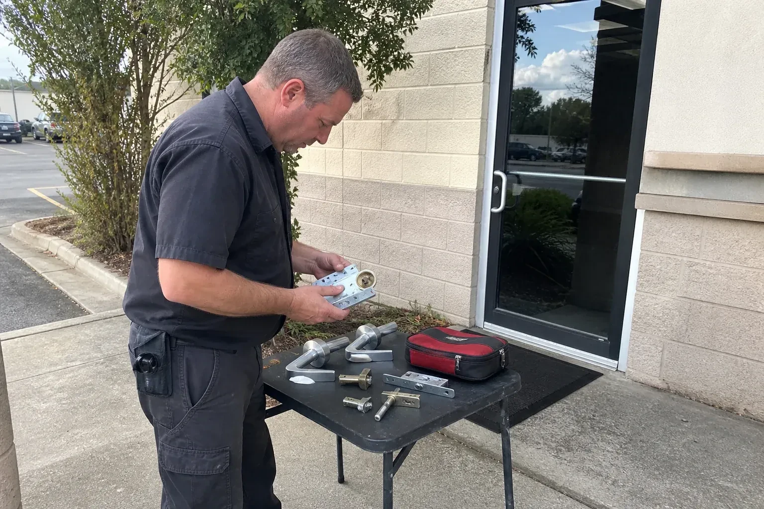 Technician examining detached commercial lock hardware on a table outside a shop entrance. — Business Lockout Service, Brantford