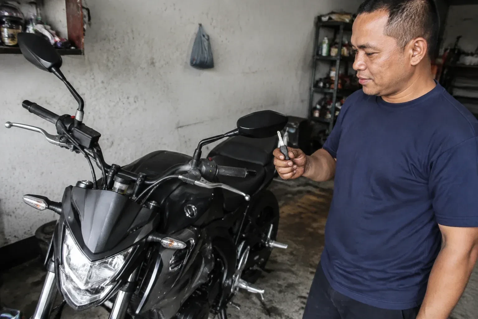 Person holding a key beside a black motorcycle in a garage. — Motorcycle & Scooter Keys, Brantford